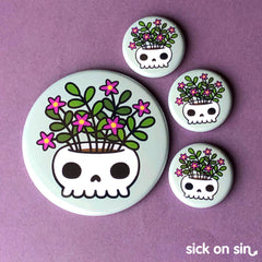 An original design of a skull planter with a plant with purple flowers planted in it. A spooky cute design by Sick On Sin available on handpressed flair like buttons, magnets, keychains, etc.