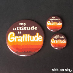 A collection of large and small buttons featuring the slogan 'my attitude is my gratitude' down in a retro font with orange and brown text treatment. A cute original design by Sick On Sin available on pins, magnets, keychains, etc.