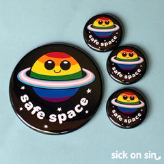 An original illustration of a smiling rainbow-colourd ringed planet with the slogan 'safe space'. This cute LGBTQ+ inclusive design by Sick On Sin is availabe on handpressed flair including pins, magnets and keychains.