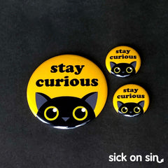 A cute design of a black cat peeking up with the slogan Stay Curious. Original artwork by Sick On Sin available on pins, magnets, keychains, etc.